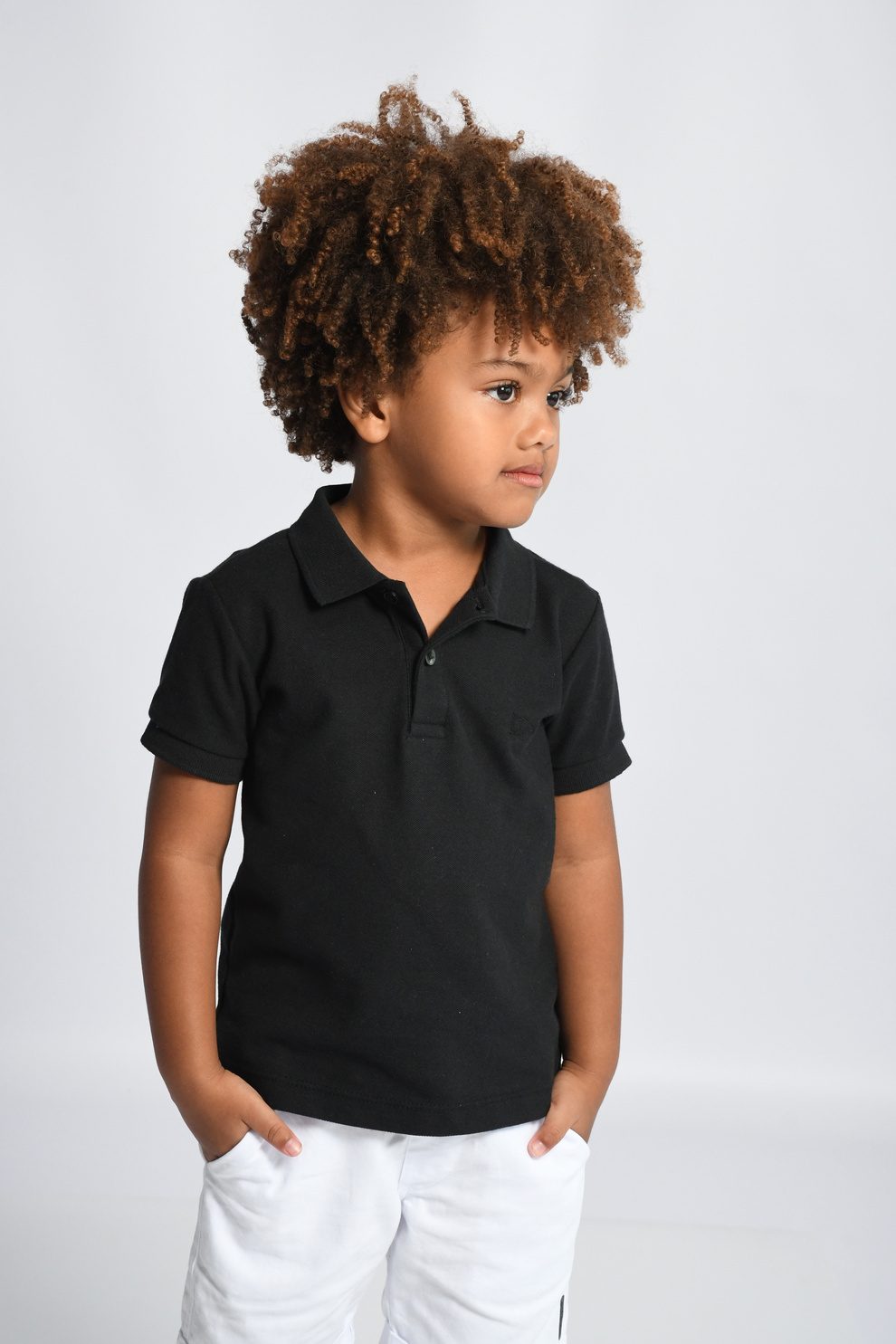 Isaac Roberto com as mãos nos bolsos, em polo preto e shorts branco, em estúdio de fundo claro