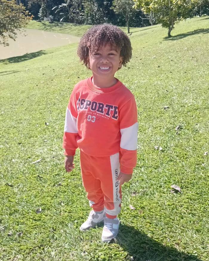 Isaac Roberto sorrindo, de moletom laranja, num gramado
