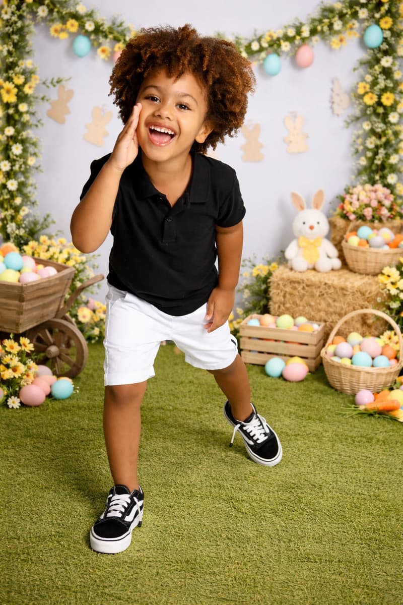 Isaac Roberto rindo, em polo preto e shorts branco, em cenário de Páscoa
