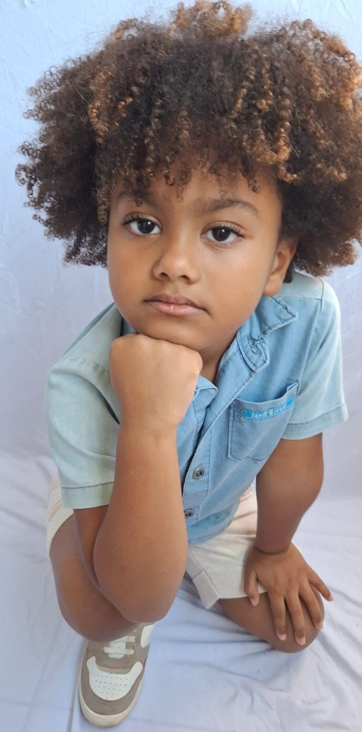 Isaac Roberto agachado com a mão no queixo, de camisa jeans clara