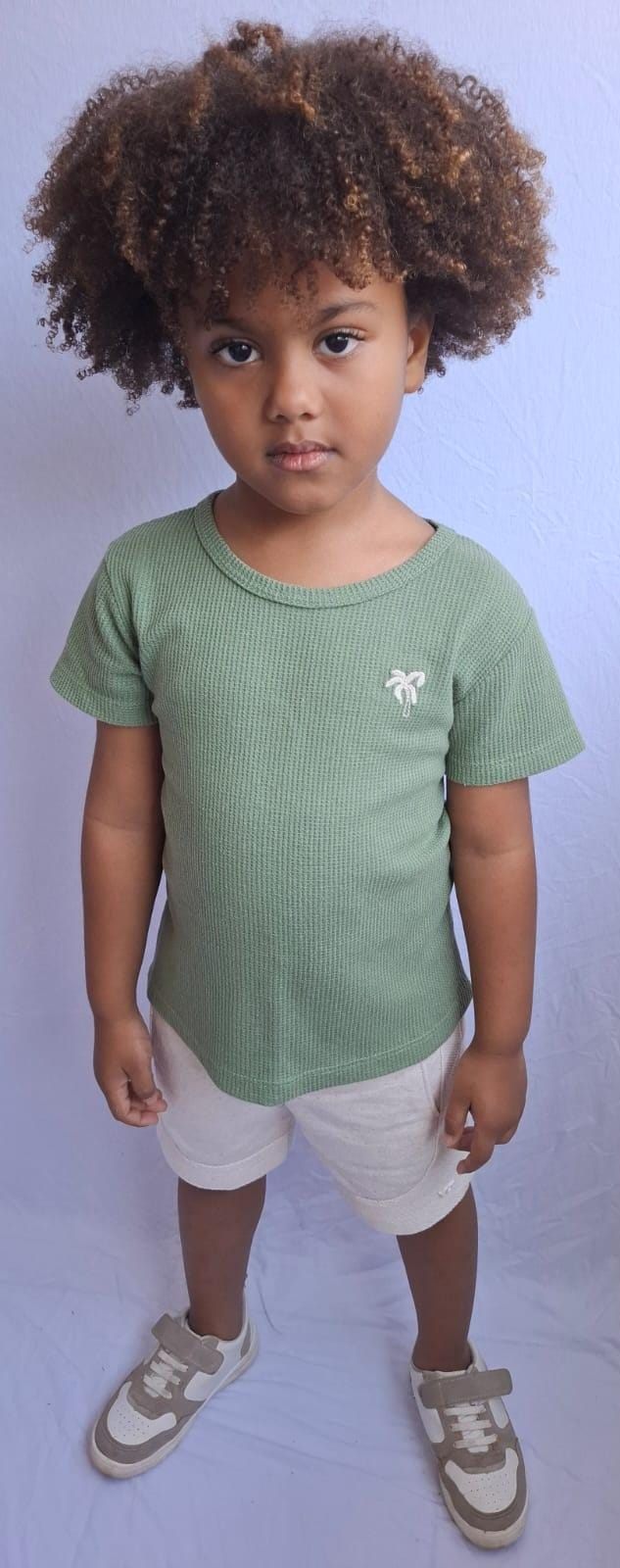 Isaac Roberto de camiseta verde e bermuda bege, em fundo claro