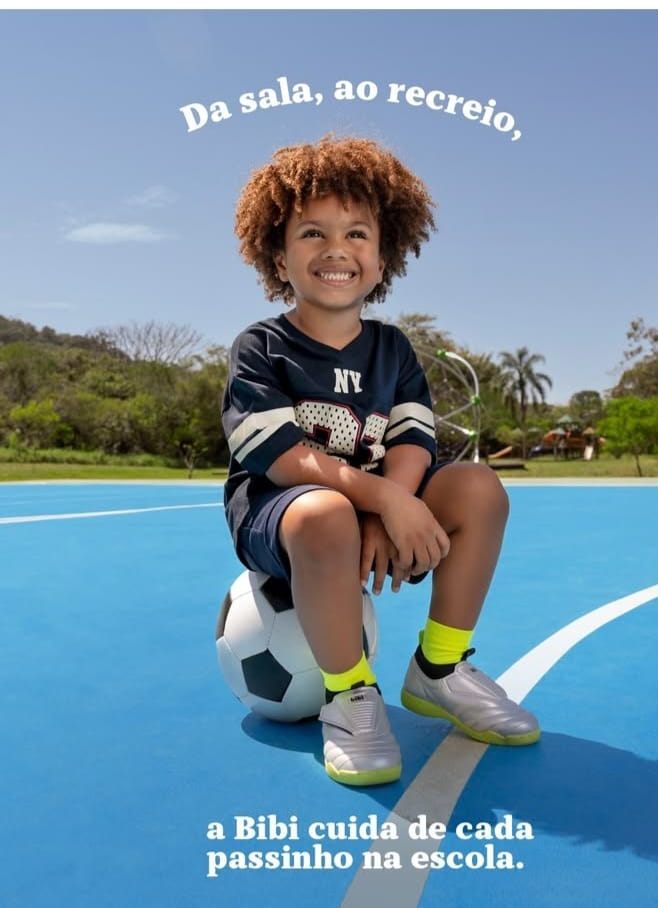 Isaac Roberto sentado numa bola de futebol, em quadra azul, na campanha da Bibi